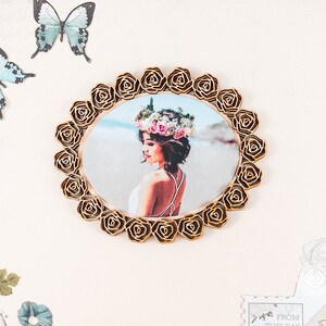 May include: A gold-coloured wooden frame with a floral design surrounds a photo of a woman wearing a flower crown. The photo shows the woman with her back to the camera, looking to the side.