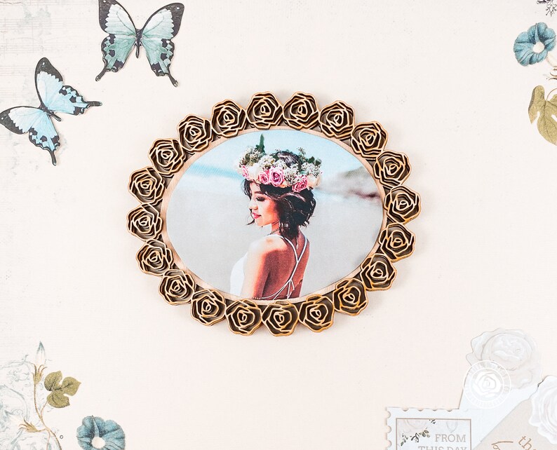 May include: A gold-coloured wooden frame with a floral design surrounds a photo of a woman wearing a flower crown. The photo shows the woman with her back to the camera, looking to the side.