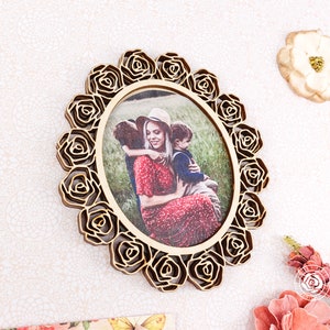 May include: A wooden photo frame with a decorative rose design. The frame is oval shaped and has a photo of a woman and two children inside.