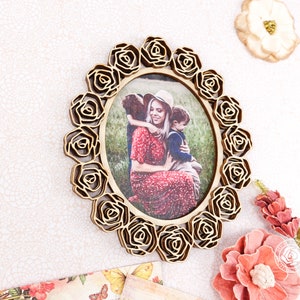 May include: A wooden picture frame with a floral design. The frame is oval shaped and has a photo of a mother and two children inside. The photo shows a woman in a red dress holding a young boy, while a young girl stands behind them.