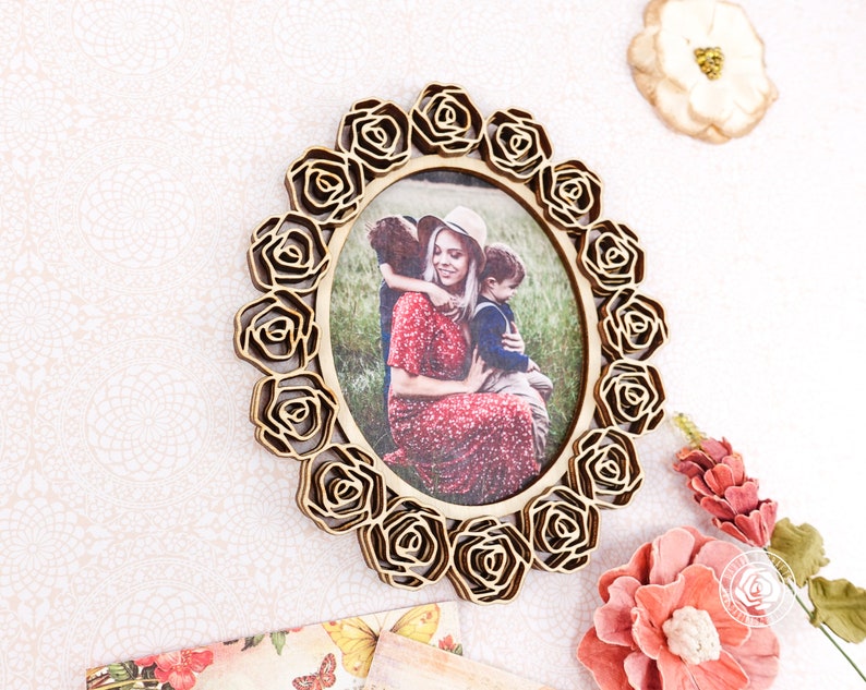 May include: A wooden picture frame with a floral design. The frame is oval shaped and has a photo of a mother and two children inside. The photo shows a woman in a red dress holding a young boy, while a young girl stands behind them.