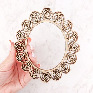 May include: A wooden frame with a circular design featuring a repeating pattern of carved roses. The frame is unfinished and ready to be painted or stained.