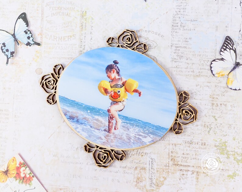 May include: A wooden photo frame with a floral design. The frame is oval shaped and has a photo of a child in a yellow life jacket standing in the ocean. The photo is surrounded by a decorative floral border.