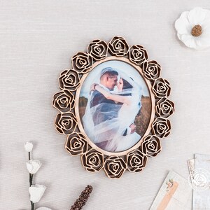May include: A wooden picture frame with a rose design. The frame is oval shaped and has a photo of a bride and groom inside. The frame is a light brown color.