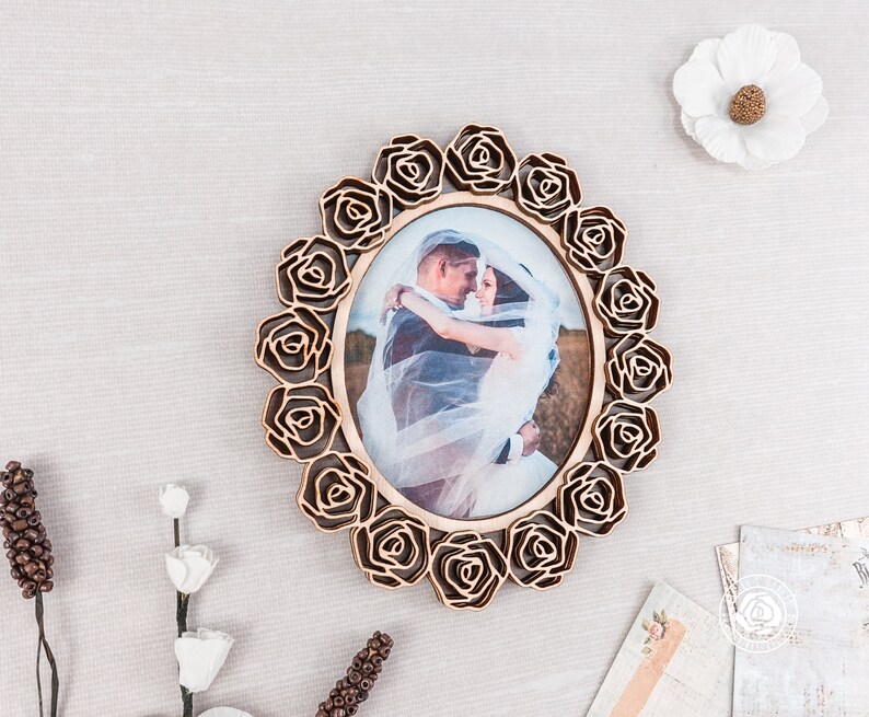 May include: A wooden picture frame with a rose design. The frame is oval shaped and has a photo of a bride and groom inside. The frame is a light brown color.
