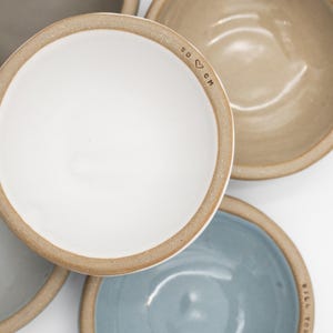May include: Overhead shot of several ceramic bowls in various colors: white, gray, tan, and blue. Each bowl has a light brown rim. The white bowl has the initials "SD ♡ CM" stamped on the rim. The blue bowl has the text "WILL YOU MARRY ME?" on the rim.