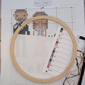 Peut inclure: Un kit de point de croix avec une toile Aida blanche, un cerceau &agrave; broder en bois, du fil &agrave; broder marron, noir et blanc, et un tableau de couleurs avec les num&eacute;ros de fil DMC.