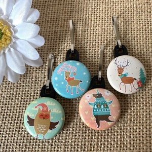 May include: Four colourful zipper pulls with different animal designs. The zipper pulls feature a reindeer, a bear, an owl, and a reindeer with antlers. The zipper pulls are made of metal and have a shiny finish.