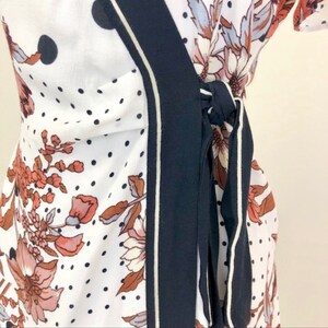 May include: A white wrap dress with a black and white polka dot pattern and a floral print. The dress has a navy blue sash with white piping that ties at the waist.