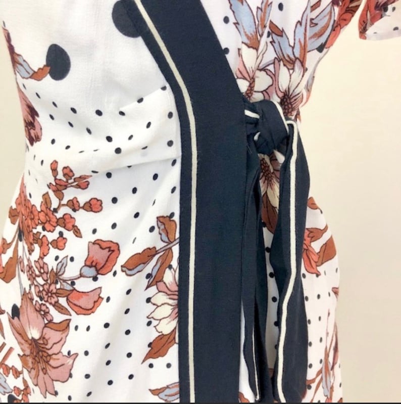 May include: A white wrap dress with a black and white polka dot pattern and a floral print. The dress has a navy blue sash with white piping that ties at the waist.