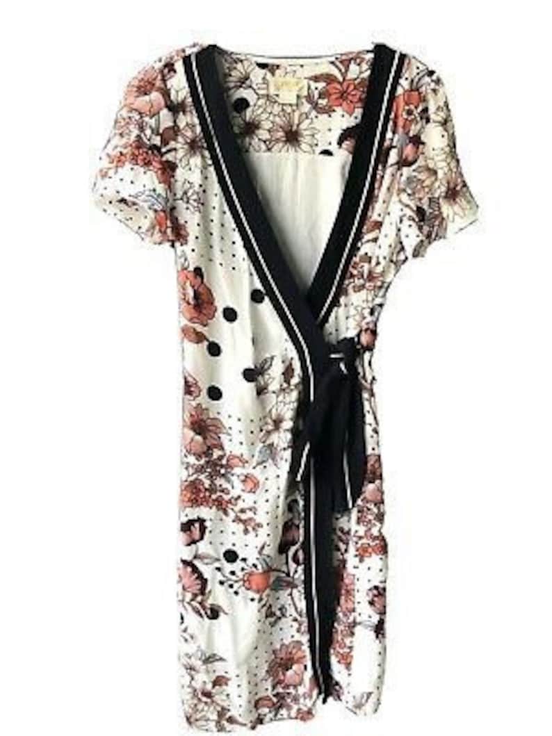 May include: A white wrap dress with a black trim and a floral print. The dress has a tie at the waist and a polka dot pattern.