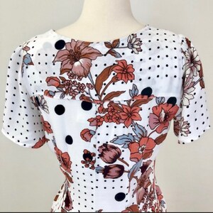 May include: White dress with a floral and polka dot pattern. The dress has short sleeves and a V-neckline.