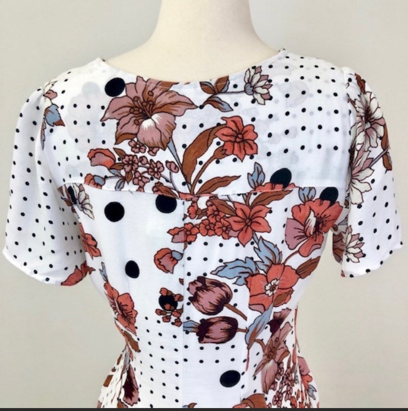 May include: White dress with a floral and polka dot pattern. The dress has short sleeves and a V-neckline.