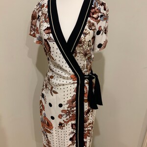 May include: A white wrap dress with a black and gold trim. The dress has a floral and polka dot pattern.