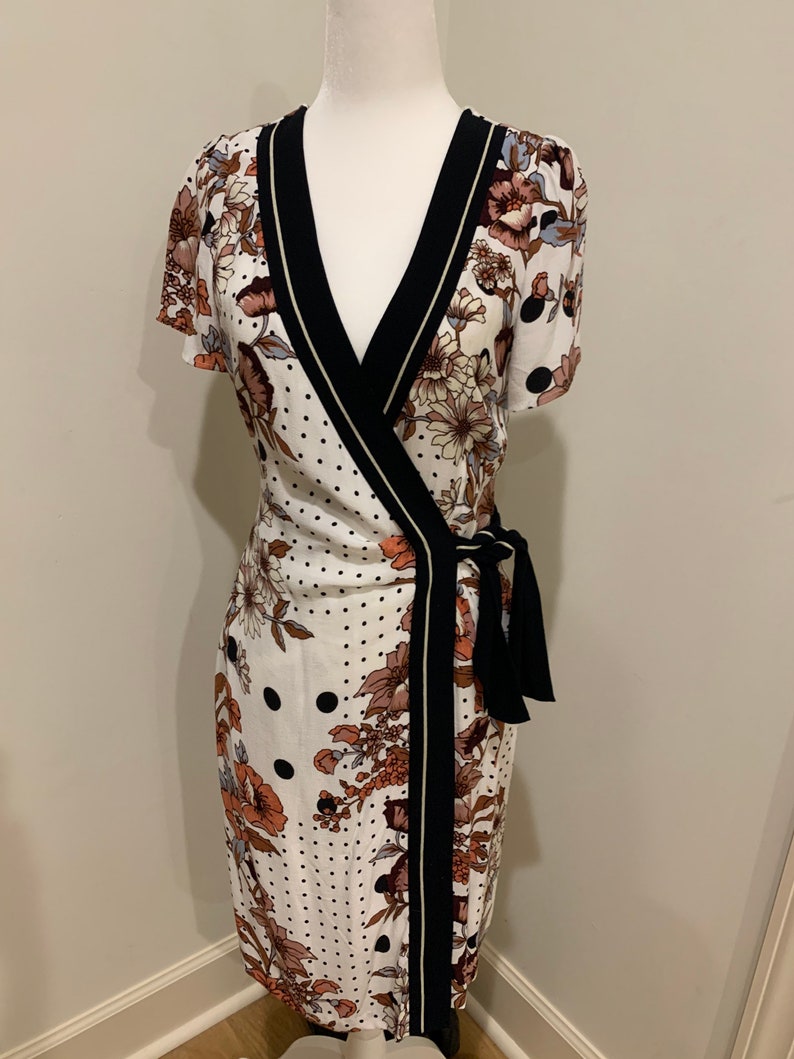 May include: A white wrap dress with a black and gold trim. The dress has a floral and polka dot pattern.
