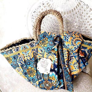 Può includere: Una borsa a mano in paglia intrecciata con stampa paisley blu e gialla. La borsa ha un'unica maniglia e una fodera nera.