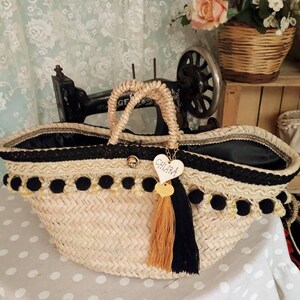 May include: A large straw tote bag with black and gold trim and black pom-poms. The bag has a black fabric lining and a heart-shaped tag that says "CHIARA".