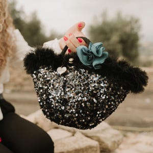 May include: A black sequined handbag with a fluffy black trim and a blue flower accent. The bag has a heart-shaped charm with the word "Love" on it.