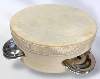 May include: A round tambourine featuring a light beige wooden frame wrapped in a matching ribbed fabric ribbon. The top surface is covered with a smooth, opaque, off-white drumhead skin, and two polished silver metal jingles are visible on the sides.