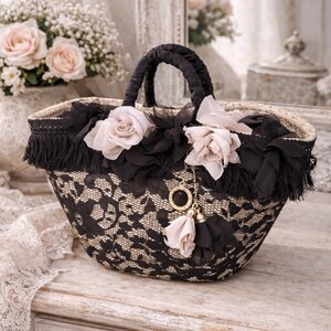 Pu&ograve; includere: Una borsa decorativa in pizzo nero e beige con manico e finiture nere. La borsa &egrave; adornata con fiori di stoffa neri e rose color rosa. Un ciondolo dorato con nappe pende dalla borsa.