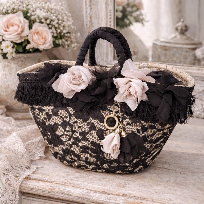 Pu&ograve; includere: Una borsa decorativa in pizzo nero e beige con manico e finiture nere. La borsa &egrave; adornata con fiori di stoffa neri e rose color rosa. Un ciondolo dorato con nappe pende dalla borsa.
