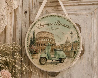 May include: A round tambourine featuring a vintage-style illustration of a light green scooter parked in front of the Roman Colosseum. The text Vacanze Romane is printed in a cursive font at the top, and the instrument is suspended by a ribbon.