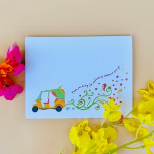 Puede incluir: Una tarjeta blanca con una ilustración colorida de un auto-rickshaw amarillo con una capota verde y un pequeño pájaro en la parte superior. El rickshaw deja un rastro de enredaderas verdes con flores rosas y patrones de cachemira. El texto "Mamá, tú traes alegría y belleza dondequiera que vayas." está escrito en rosa.