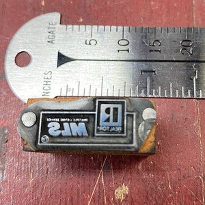 May include: A wooden stamp with a silver metal face. The stamp reads "REALTOR" and "MLS" with a blue and silver logo of a house with the letter "R" inside.