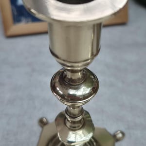 Peut inclure: Un bougeoir en m&eacute;tal argent&eacute; poli dot&eacute; d'une ouverture circulaire sur le dessus, d'une tige fine avec des n&oelig;uds d&eacute;coratifs arrondis et facett&eacute;s, et d'une base carr&eacute;e reposant sur de petits pieds arrondis &agrave; chaque coin de la structure.