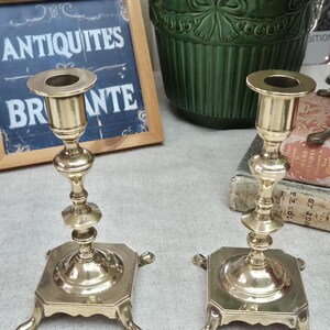 Peut inclure: Une paire de bougeoirs en laiton poli dot&eacute;s d'une tige fine &agrave; plusieurs niveaux et d'une base carr&eacute;e soutenue par quatre pieds incurv&eacute;s. Chaque bougeoir pr&eacute;sente une ouverture circulaire sup&eacute;rieure con&ccedil;ue pour maintenir une bougie.