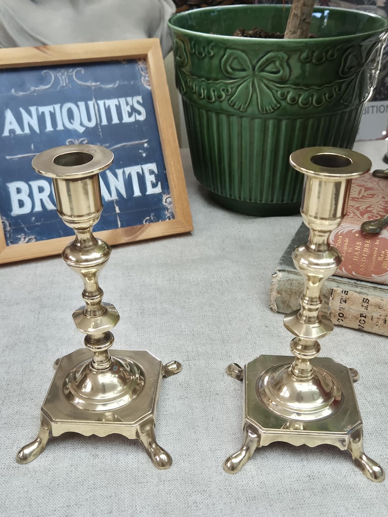 Peut inclure: Une paire de bougeoirs en laiton poli dot&eacute;s d'une tige fine &agrave; plusieurs niveaux et d'une base carr&eacute;e soutenue par quatre pieds incurv&eacute;s. Chaque bougeoir pr&eacute;sente une ouverture circulaire sup&eacute;rieure con&ccedil;ue pour maintenir une bougie.