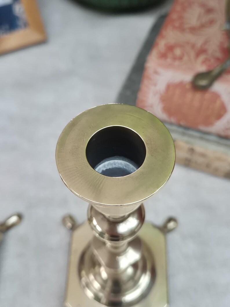 Peut inclure: Un bougeoir en laiton poli dot&eacute; d'une ouverture circulaire sur le dessus, d'une tige centrale fine avec des n&oelig;uds arrondis d&eacute;coratifs et d'une base carr&eacute;e avec de petits pieds saillants &agrave; chaque coin, vu en plong&eacute;e.