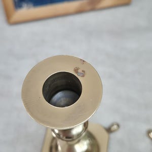 Peut inclure: Un bougeoir en laiton dot&eacute; d'un sommet circulaire avec une ouverture centrale pour une bougie. La surface m&eacute;tallique pr&eacute;sente une finition polie avec une petite zone de d&eacute;coloration sur le bord. La base du bougeoir est hexagonale.