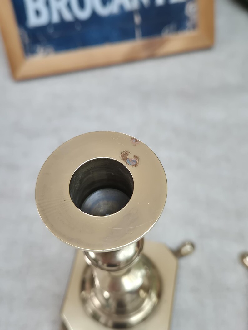 Peut inclure: Un bougeoir en laiton dot&eacute; d'un sommet circulaire avec une ouverture centrale pour une bougie. La surface m&eacute;tallique pr&eacute;sente une finition polie avec une petite zone de d&eacute;coloration sur le bord. La base du bougeoir est hexagonale.