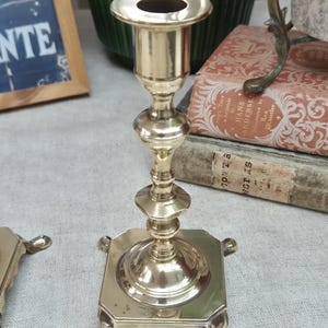 Peut inclure: Un bougeoir en laiton poli dot&eacute; d'une tige haute et fine avec plusieurs anneaux d&eacute;coratifs et un sommet &eacute;vas&eacute;. La base est de forme carr&eacute;e avec quatre pieds incurv&eacute;s et saillants qui assurent la stabilit&eacute; de la structure m&eacute;tallique.