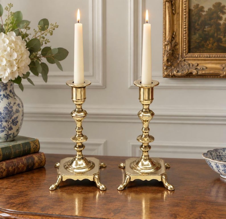 Peut inclure: Une paire de bougeoirs en laiton poli avec des bases carr&eacute;es et quatre pieds, chacun portant une longue bougie effil&eacute;e blanc cass&eacute;. Les supports en m&eacute;tal pr&eacute;sentent un design &agrave; tige tourn&eacute;e &agrave; plusieurs niveaux avec une finition lisse.