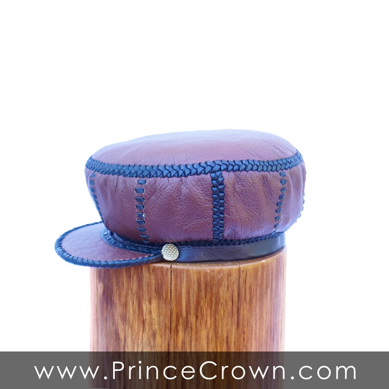 May include: A brown leather cap with black stitching and a black leather band. The cap is sitting on a wooden stand.
