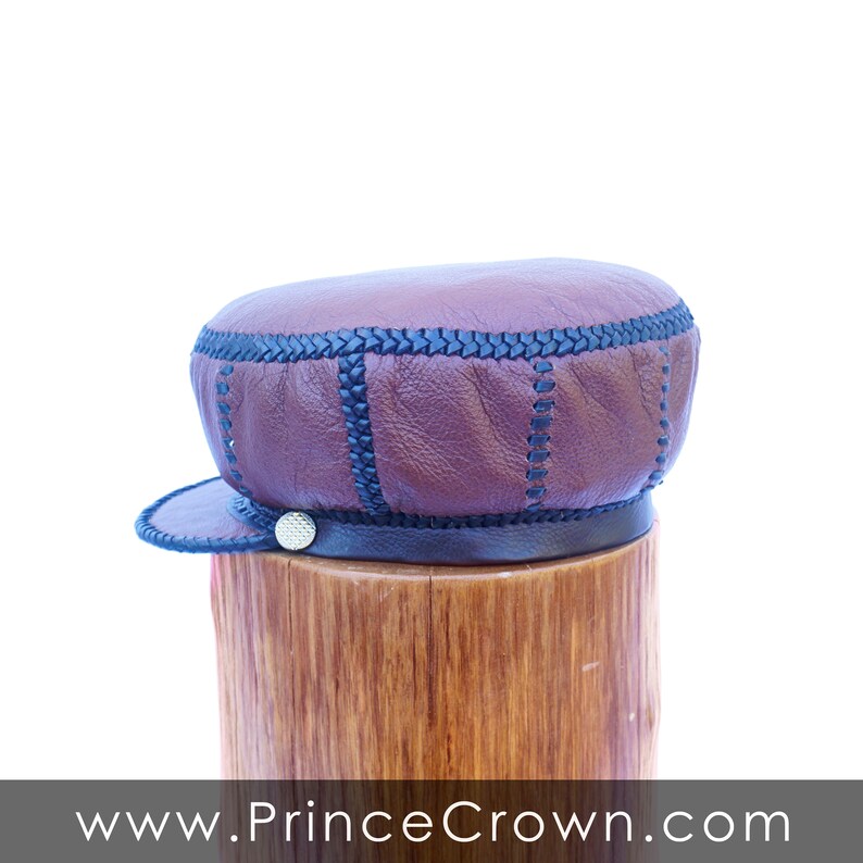 May include: A brown leather cap with black stitching and a black band around the bottom. The cap is sitting on a wooden surface.
