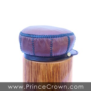 May include: A brown leather cap with black stitching and a gold button. The cap is sitting on a wooden stand.