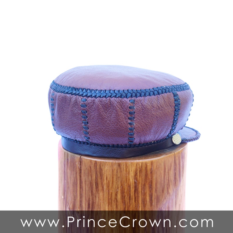 May include: A brown leather cap with black stitching and a gold button. The cap is sitting on a wooden stand.