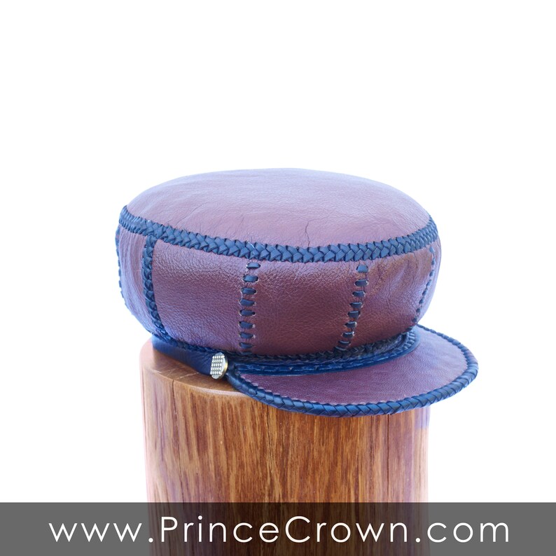 May include: A brown leather cap with black stitching and a black leather brim. The cap has a gold button on the front.