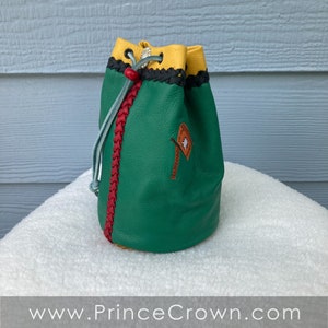 May include: A green leather dice bag with yellow, red, and black trim. The bag has a drawstring closure and a small embroidered design on the front.