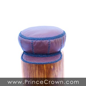 May include: A brown leather hat with a black stitched brim. The hat is sitting on a wooden surface.