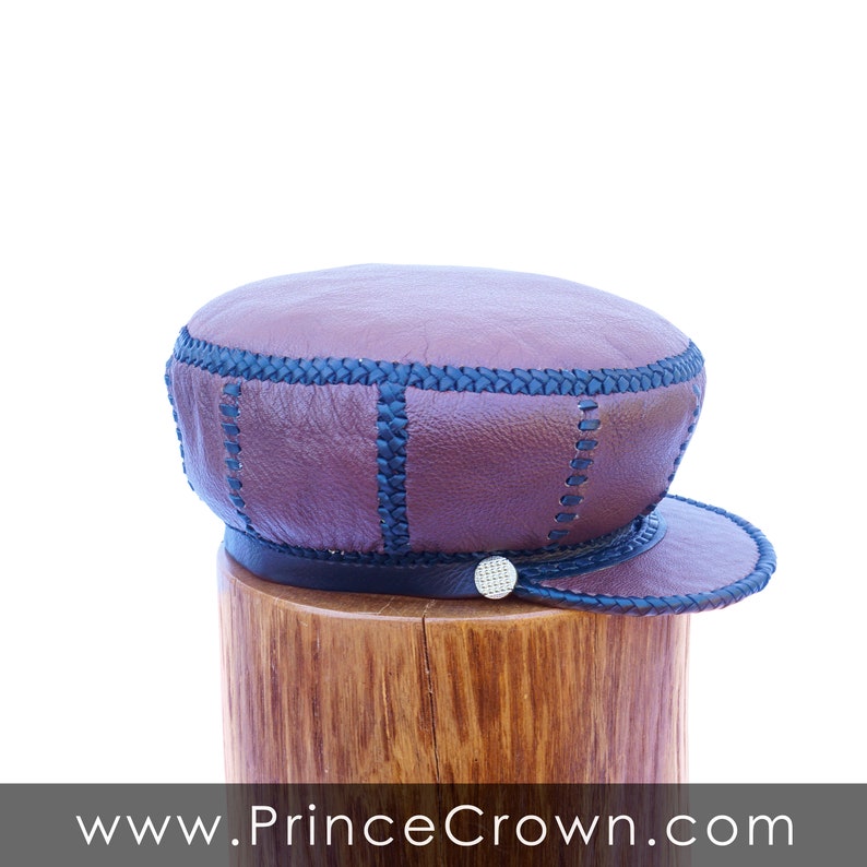 May include: A brown leather cap with black stitching and a small silver button on the side. The cap is sitting on a wooden surface.