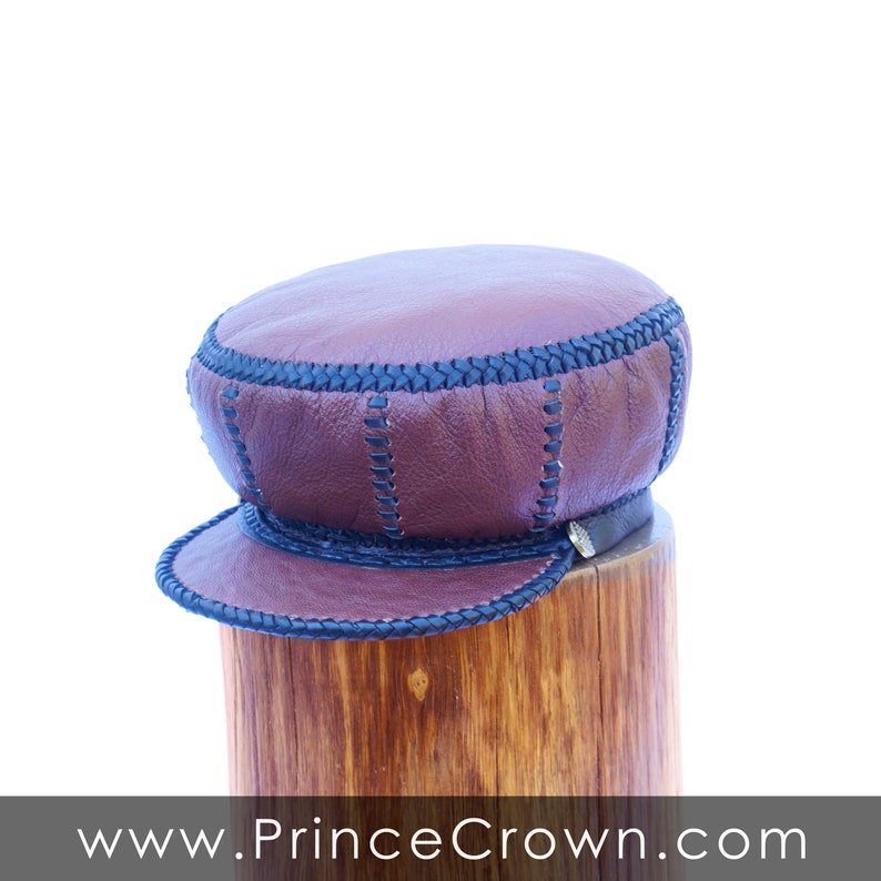 May include: A brown leather cap with black stitching and a brim. The cap is sitting on a wooden surface.