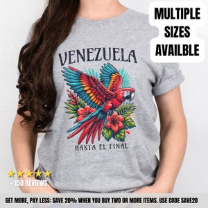May include: Gray t-shirt with a red, yellow, and blue parrot flying over tropical flowers and leaves. The text "Venezuela" is above the parrot and "Hasta El Final" is below the parrot. The text "Multiple Sizes Available" is in the upper right corner of the image.