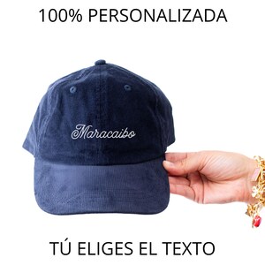 May include: Navy blue corduroy baseball cap with the word "Maracaibo" embroidered in white script. The text "100% PERSONALIZED" and "T&Uacute; ELIGES EL TEXTO" are above and below the cap.