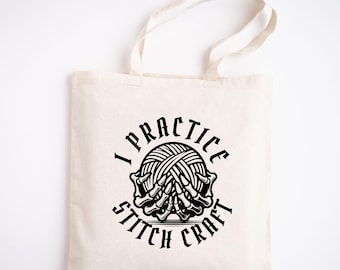 May include: A white tote bag with black text that reads "I practice stitch craft". The text is in a circle with a skeleton hand holding a ball of yarn in the center.