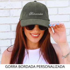 May include: Olive green corduroy baseball cap with the embroidered word "Maracaibo" in white script. The cap has a curved brim and a fabric-covered button on top. The text "GORRA BORDADA PERSONALIZADA" is at the bottom of the image.
