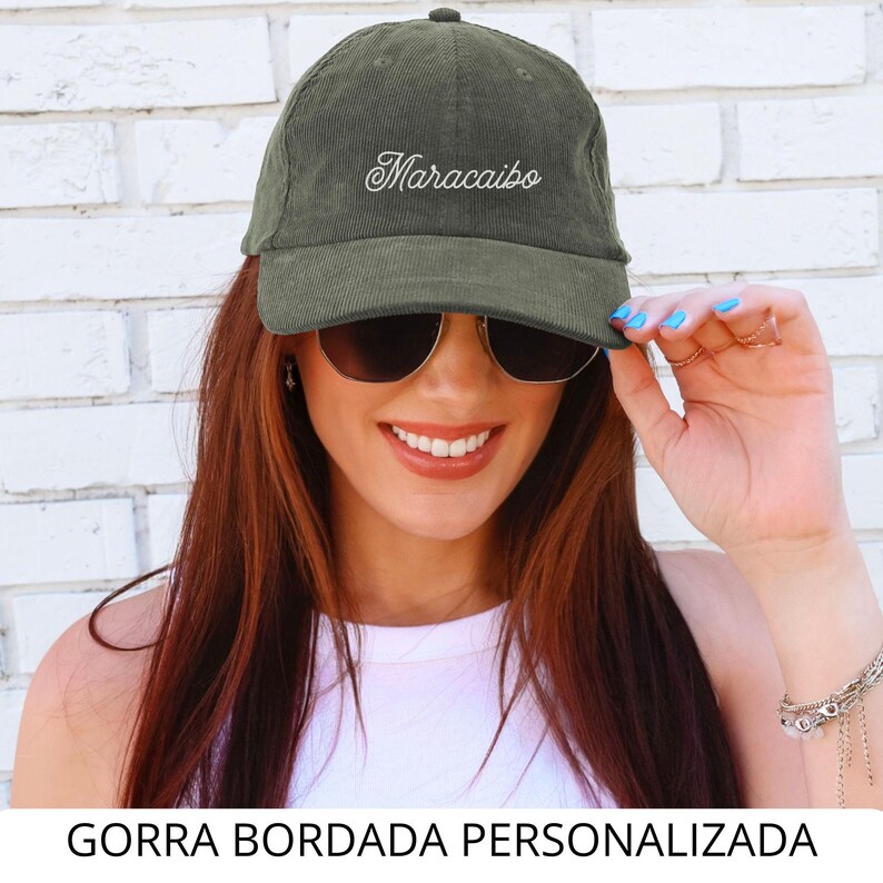 May include: Olive green corduroy baseball cap with the embroidered word "Maracaibo" in white script. The cap has a curved brim and a fabric-covered button on top. The text "GORRA BORDADA PERSONALIZADA" is at the bottom of the image.